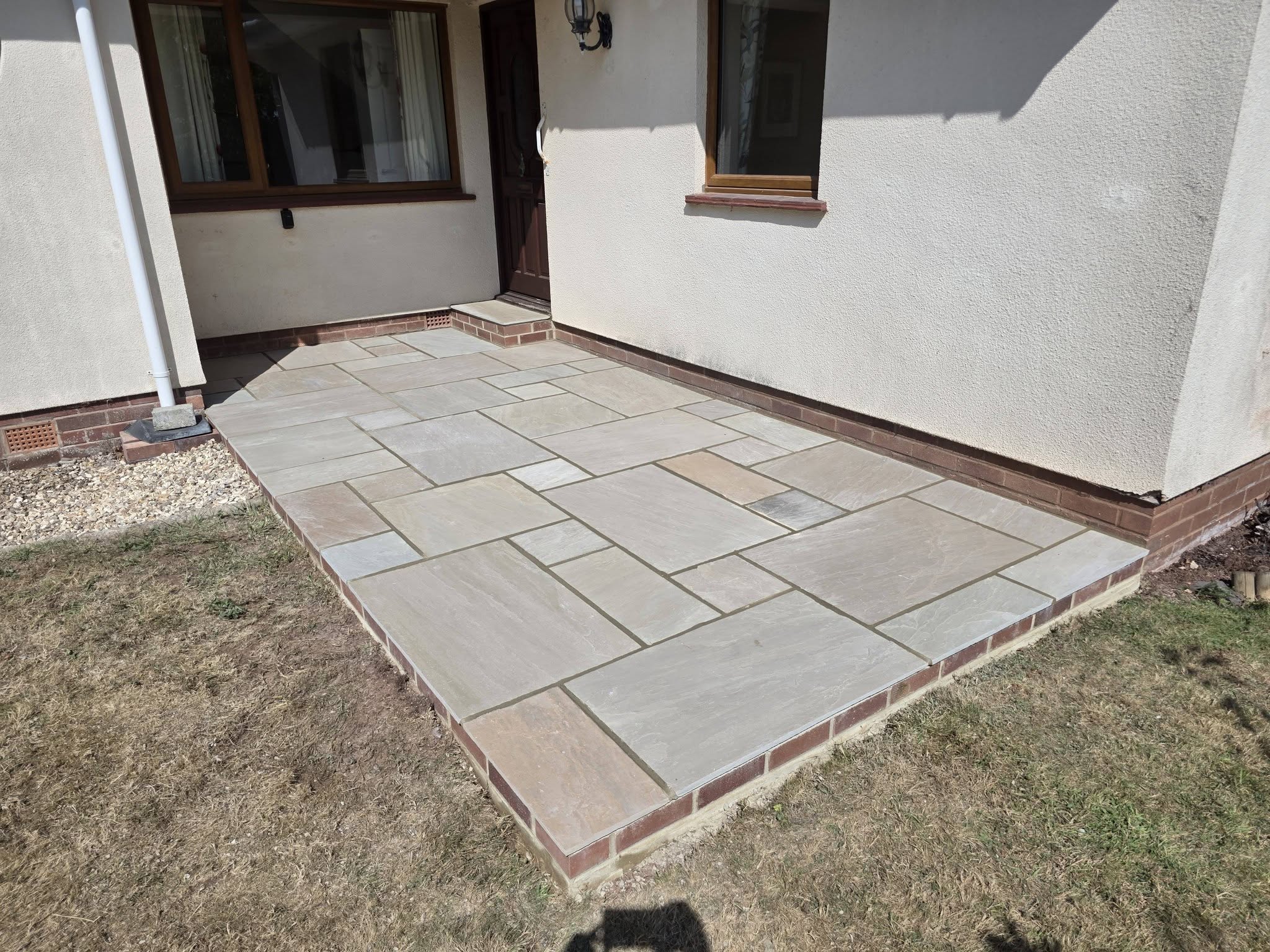 Stone patio with brick edging against a white rendered bungalow