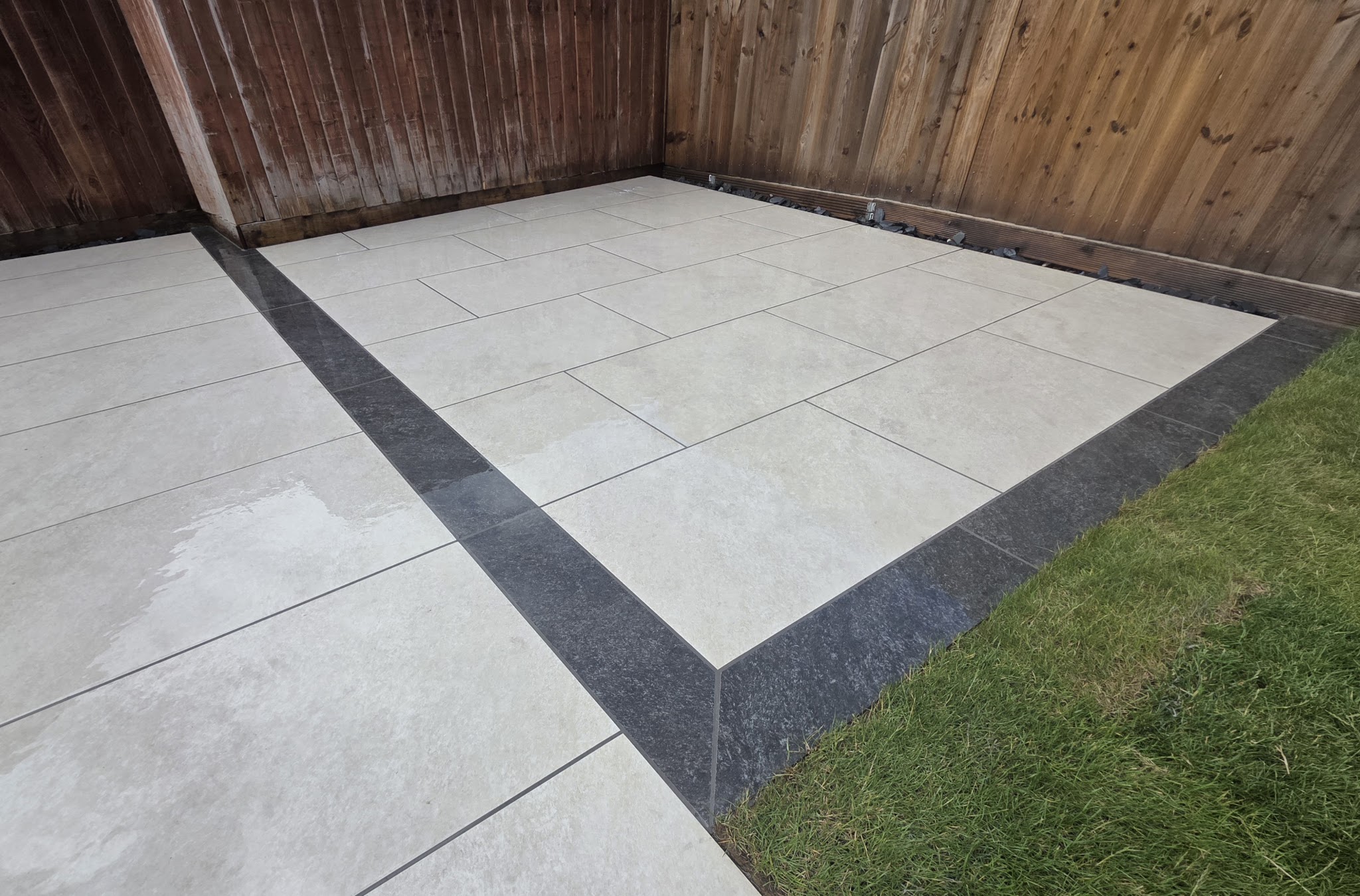 Light grey patio with a dark border strip, timber fence and lawn edge