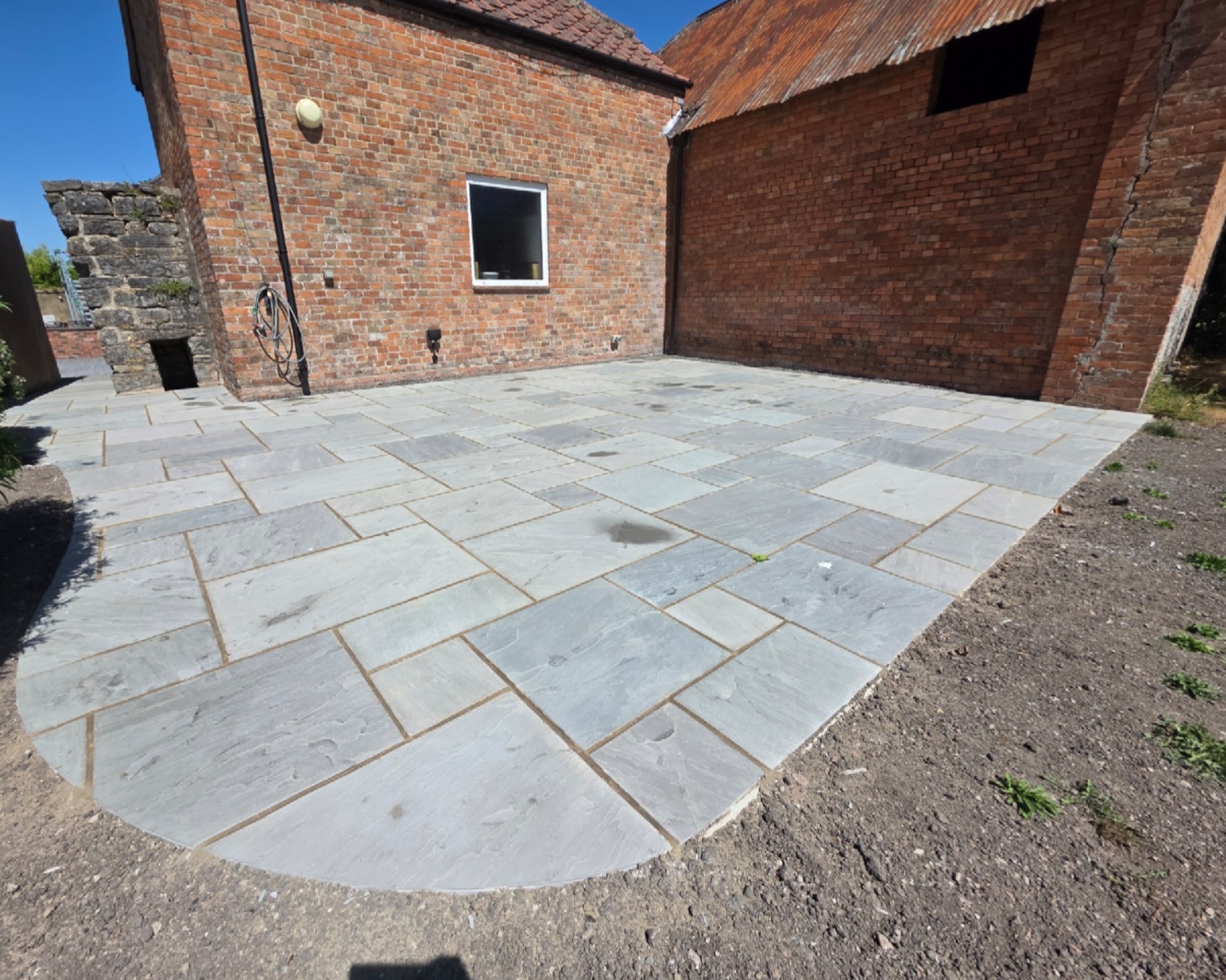 After: the same courtyard finished in grey stone paving with a curved edge