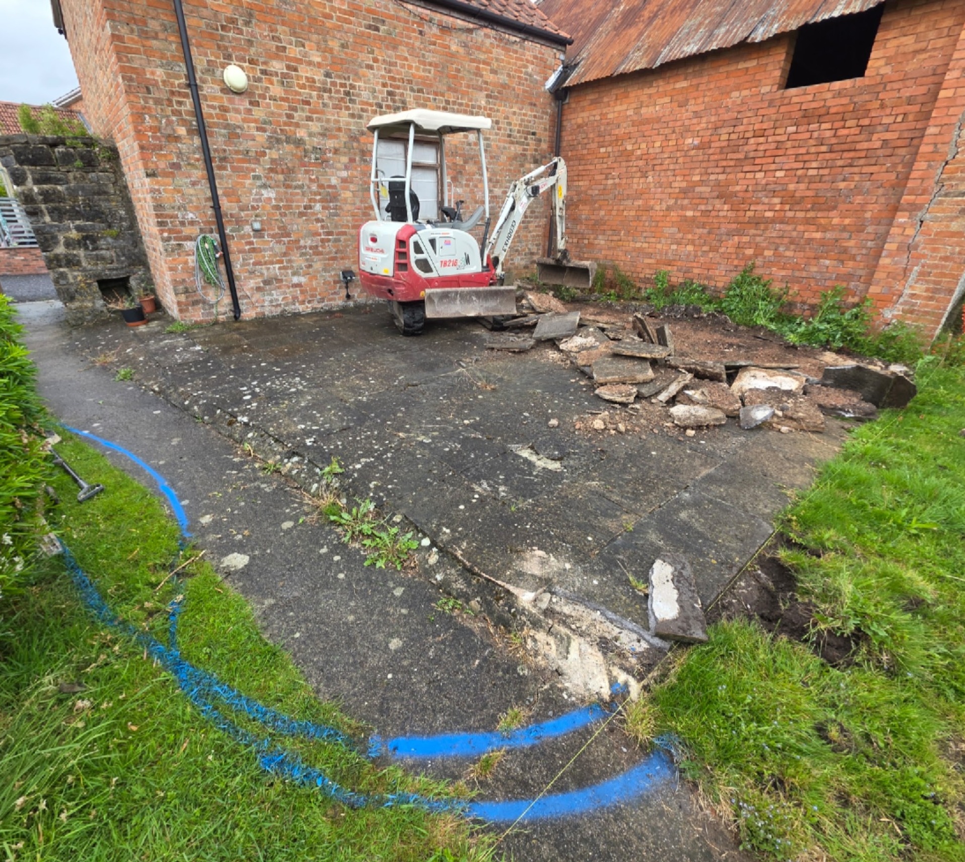 Before: broken concrete yard beside old red-brick walls, with a mini digger on site