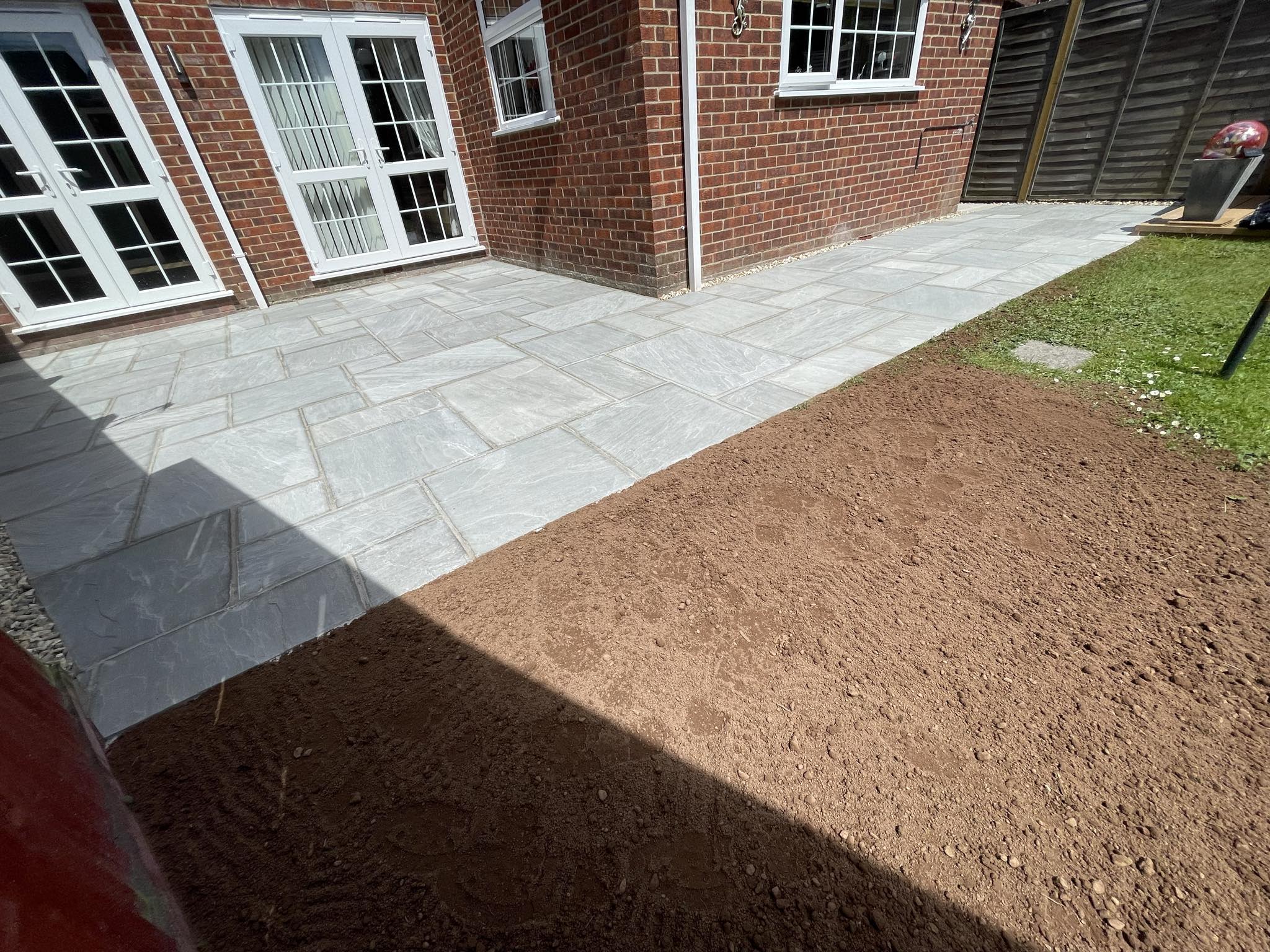 Grey stone patio running along the back of a brick house, with the soil beside it levelled