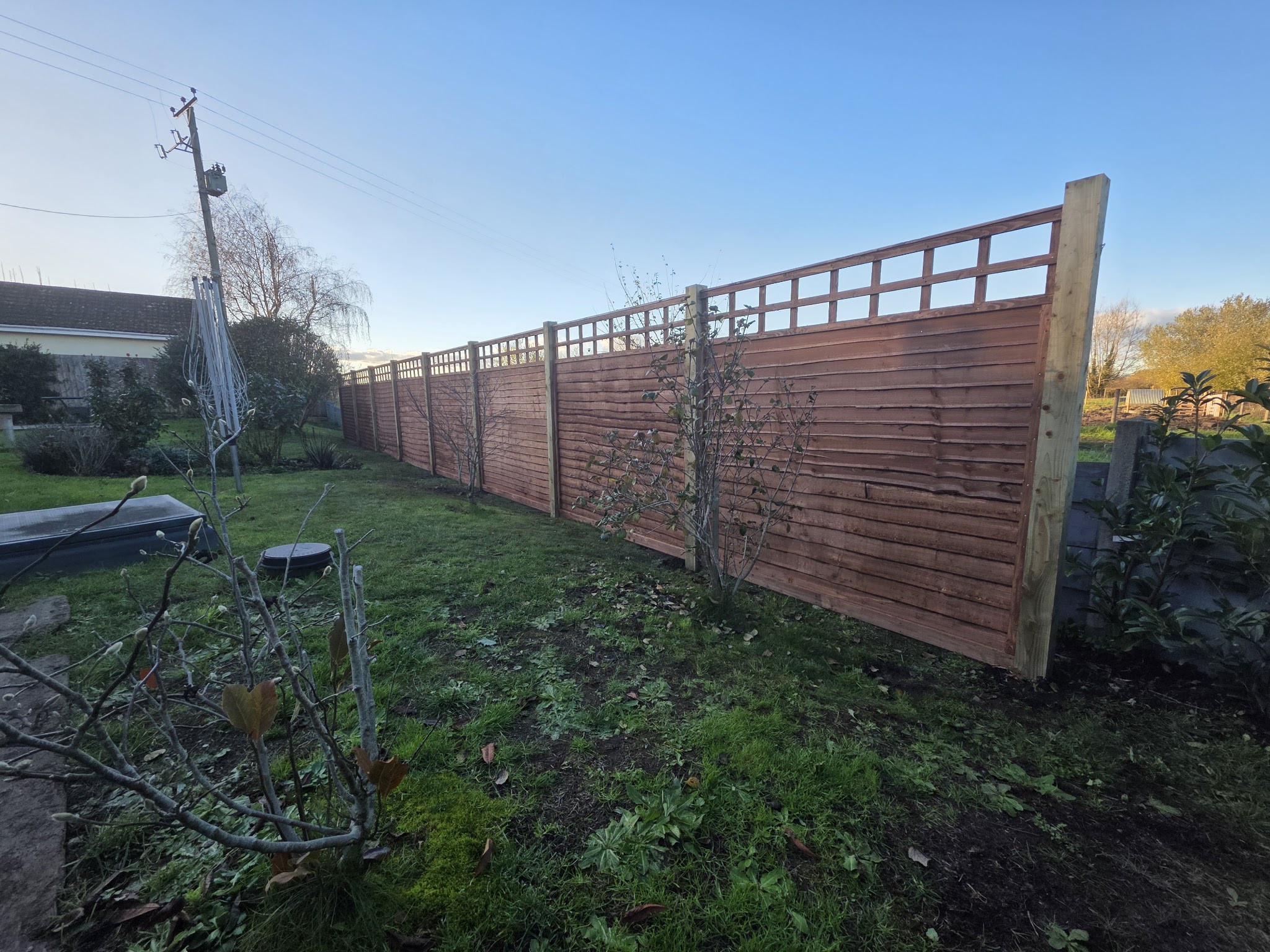 Long run of new horizontal-slat fence panels with trellis tops in a rural garden