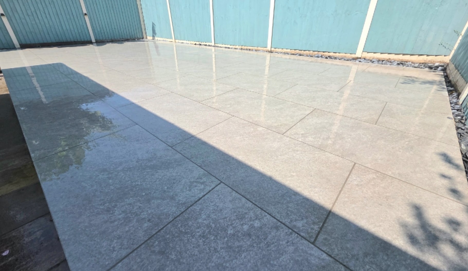 Large pale patio, freshly washed, in front of a duck-egg blue fence