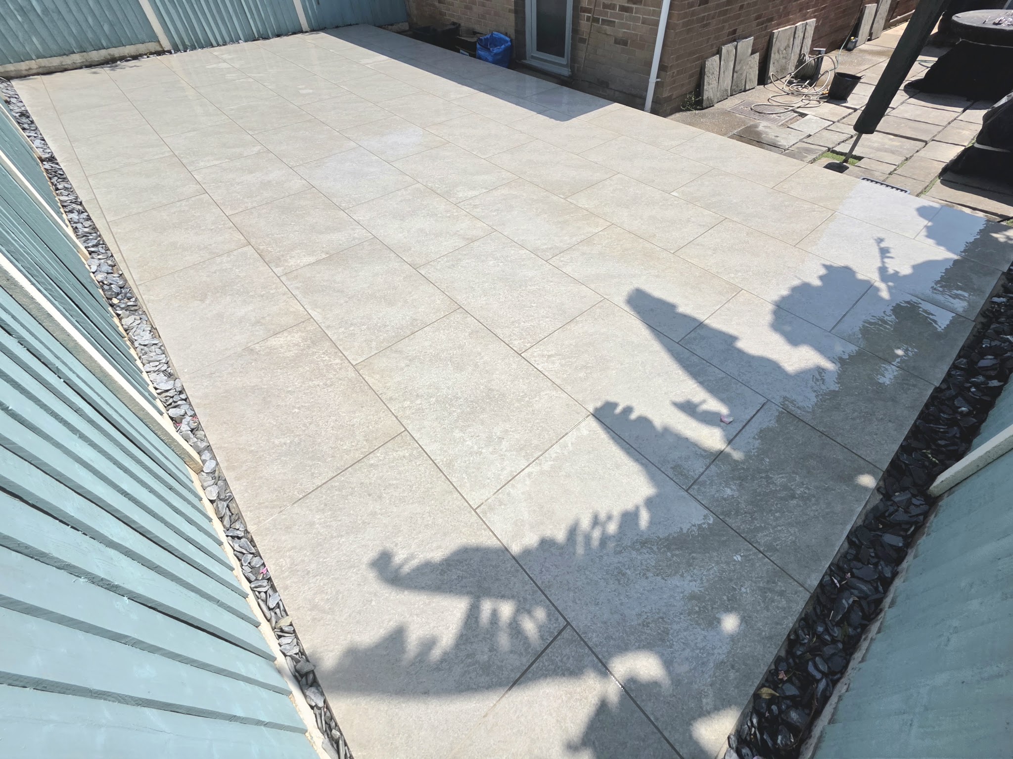 Pale patio with a slate chipping edge beside a blue fence